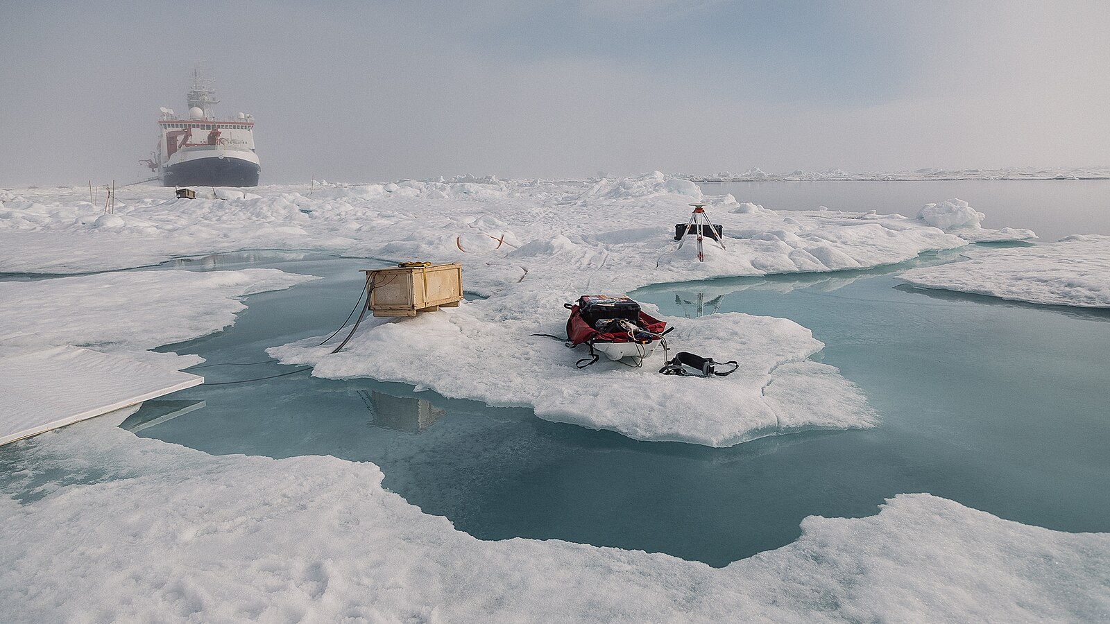 "Meltwater MOSAiC" by Evgenii Salganik. Research vessel Polarstern in the background, foreground shows equipment on sea ice and meltwater. 